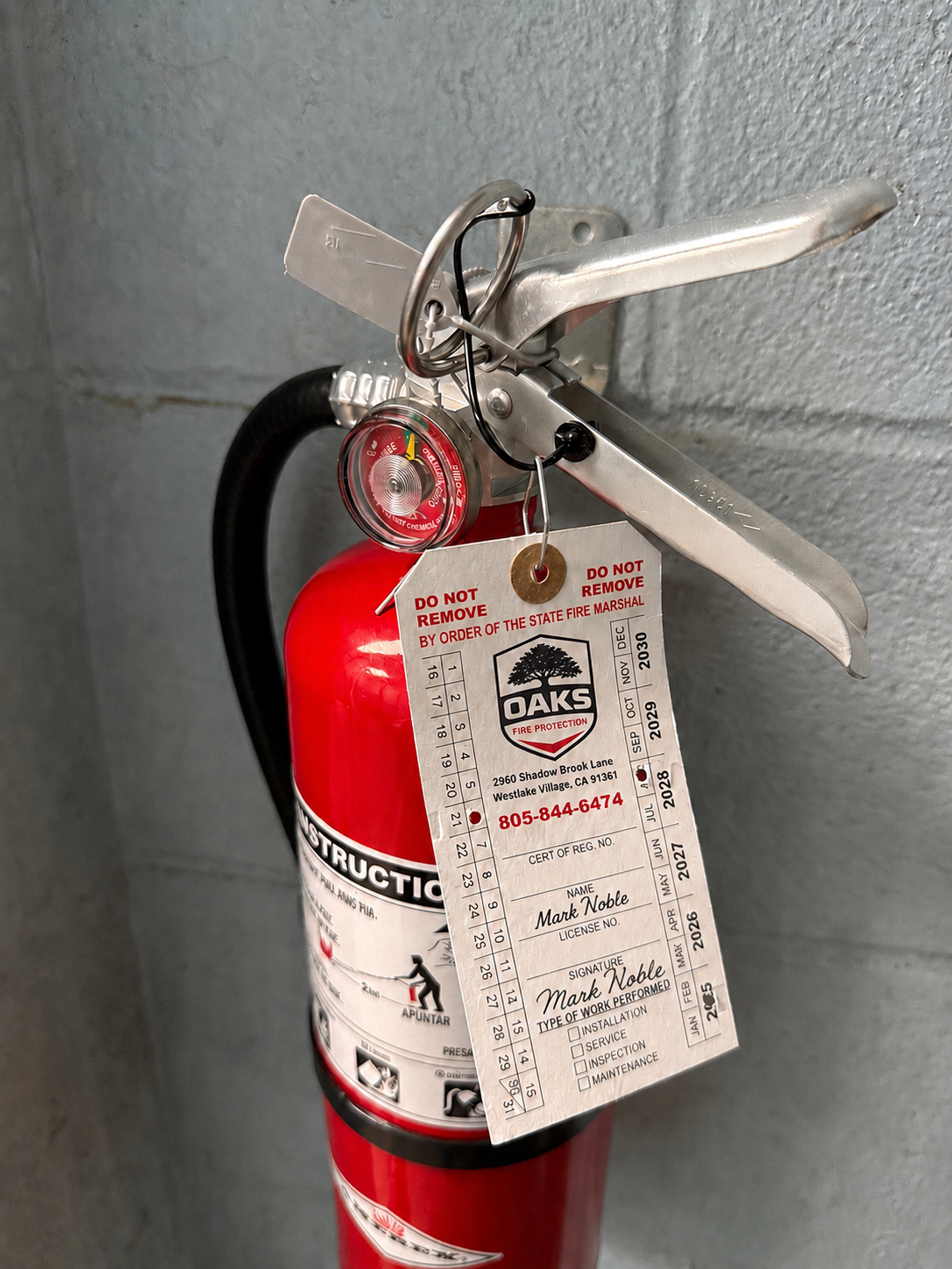 Red fire extinguisher with an Oaks Fire Protection inspection tag